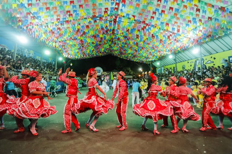 Quadrilha junina dançando numa quadra enfeitada com bandeirinhas