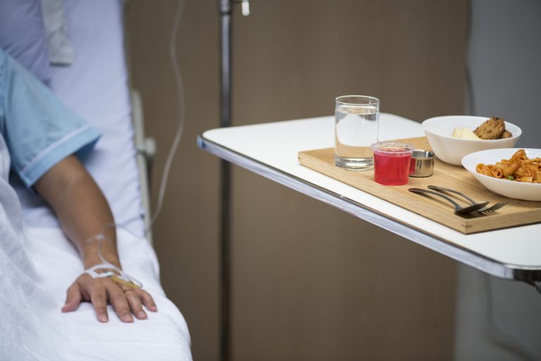 Paciente deitado numa maca com soro. Ao lado uma mesa com comida