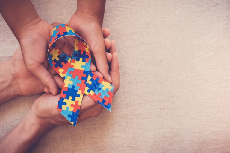 Mãos sobrepostas seguram um laço de fita com o desenho de quebra-cabeça colorido