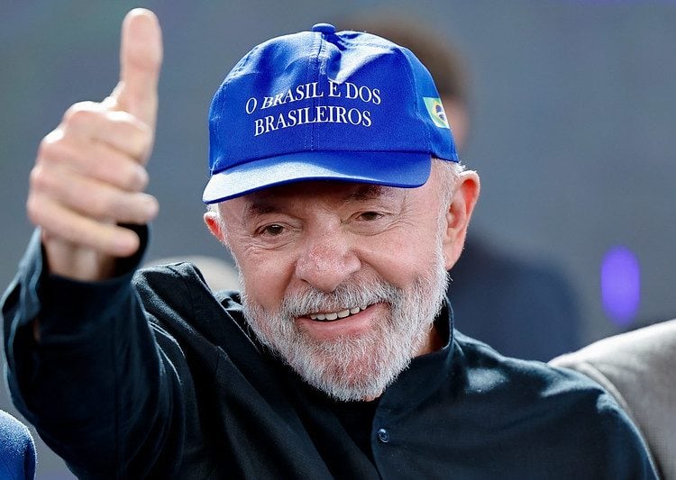 Com um boné azul onde se lê, o Brasil é dos Brasileiros, Lula faz sinal de "tudo certo" com o polegar direito